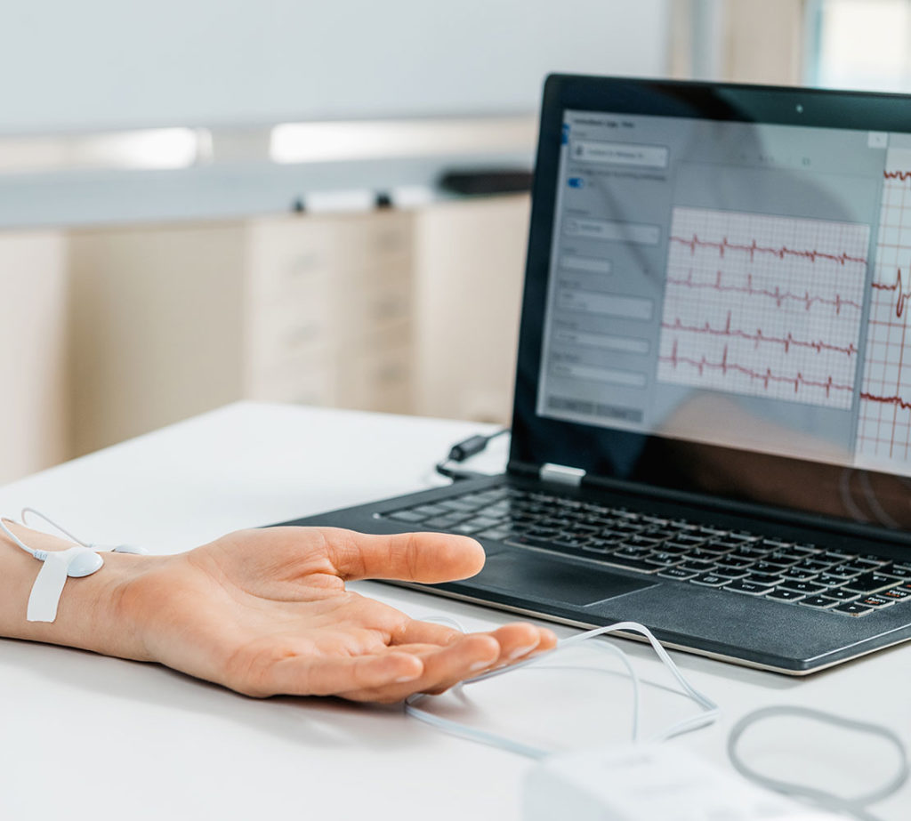A close-up shot of a patient using a digital monitoring device connected to a laptop showing the signals.